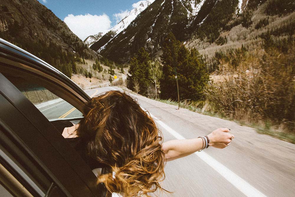 Woman with head our of the window getting fresh air as she drives through the mountains with her husband.   Feeling refresh after taking her Mtiva CBD day CBD Oil.  